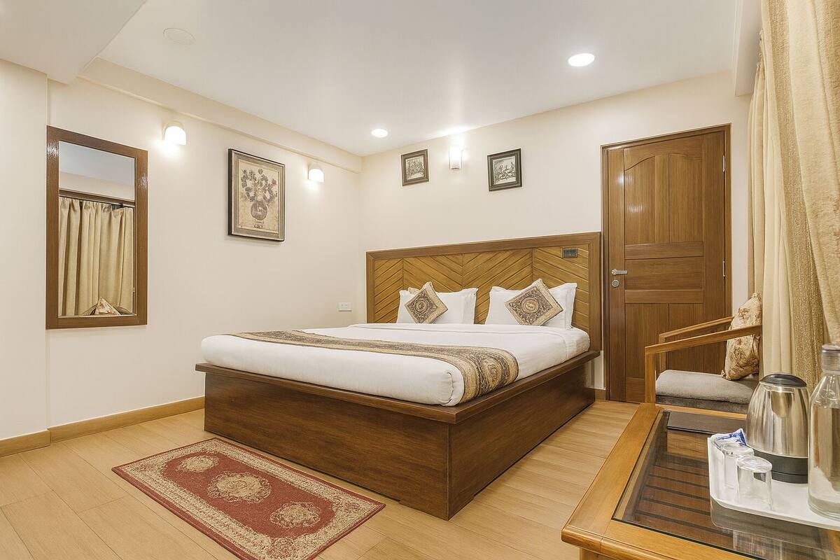 Habitación de hotel con una cama y mesita de noche de madera, un espejo, una puerta y una alfombra roja estampada.