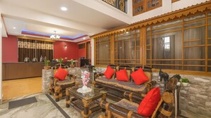 A lobby with a reception desk, seating area with cushioned chairs, a glass coffee table, and a decorative vase. - Hotel White Yak (Darjeeling)