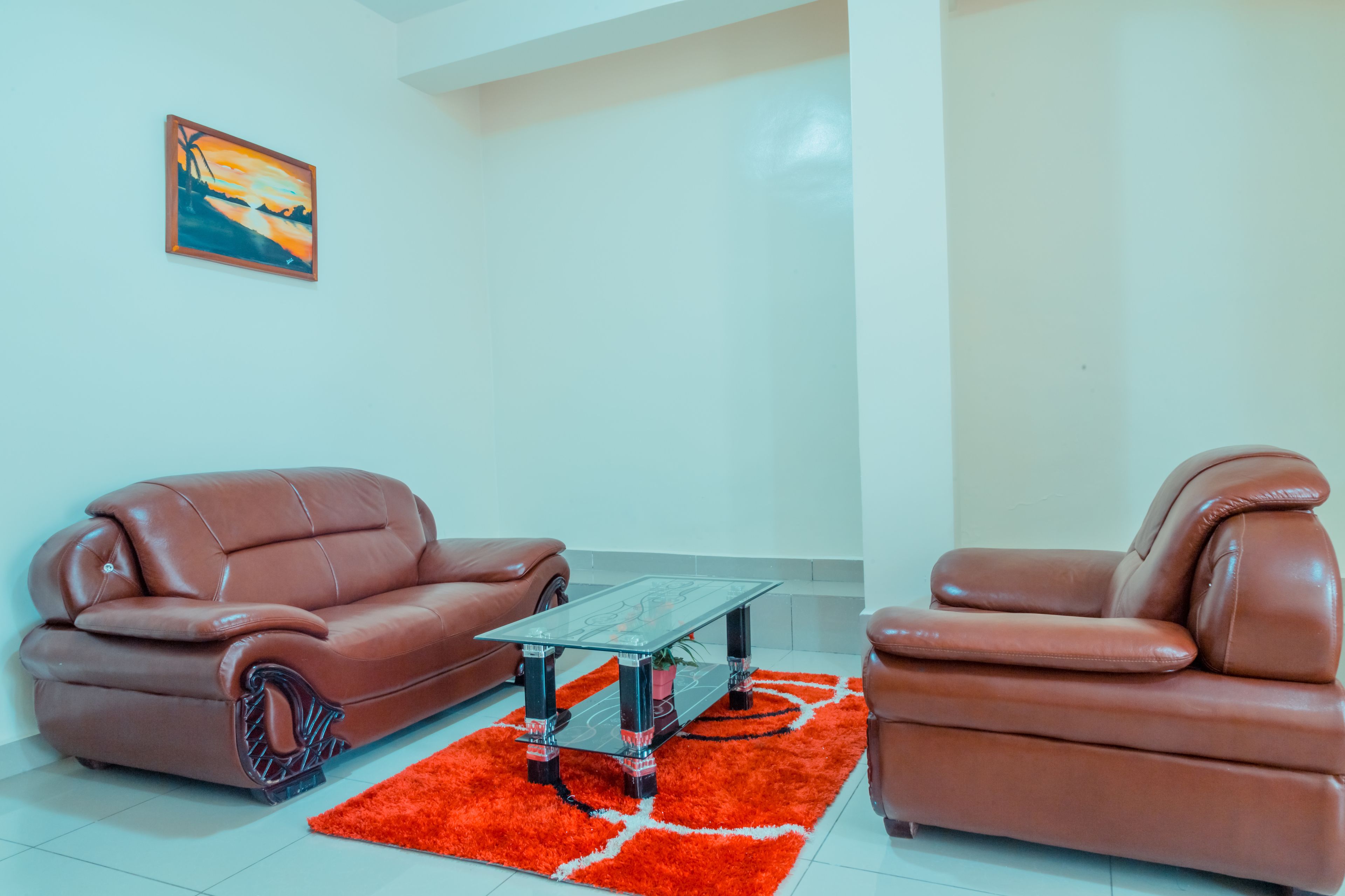 A living room with a brown leather sofa, a glass coffee table, and a red rug.