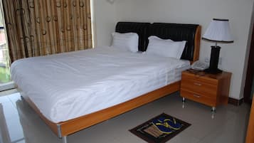 Una cama bien hecha con sábanas blancas, una mesita de noche de madera con una lámpara y un teléfono.