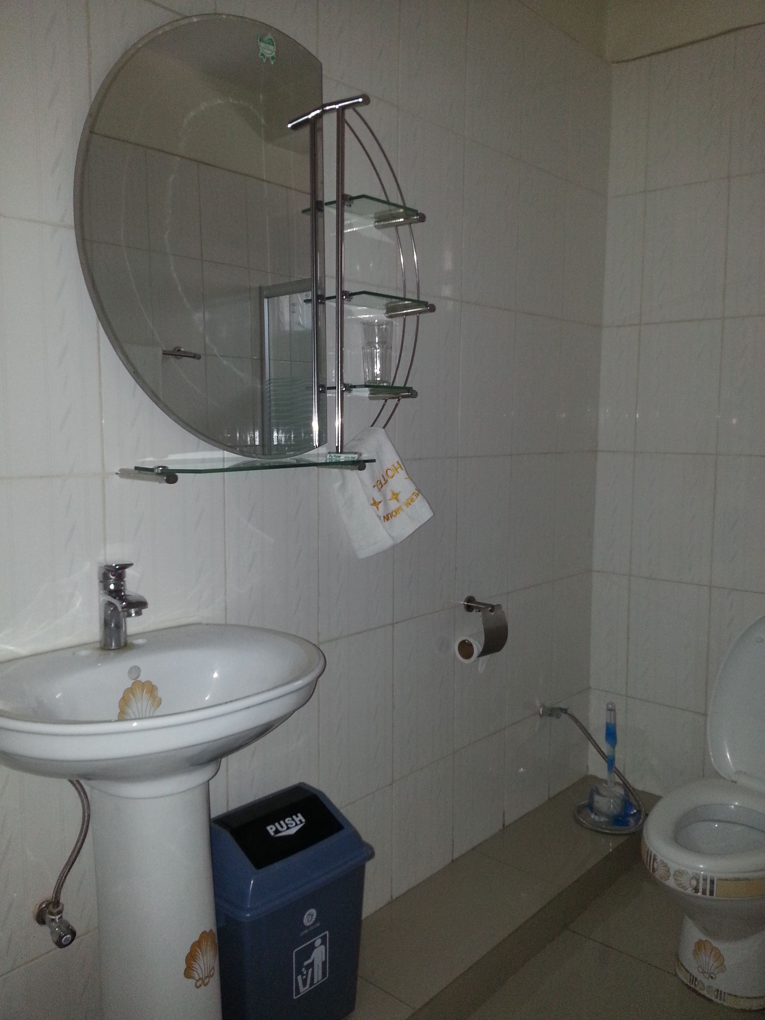 A bathroom with a sink, mirror, toilet, and a trash bin.