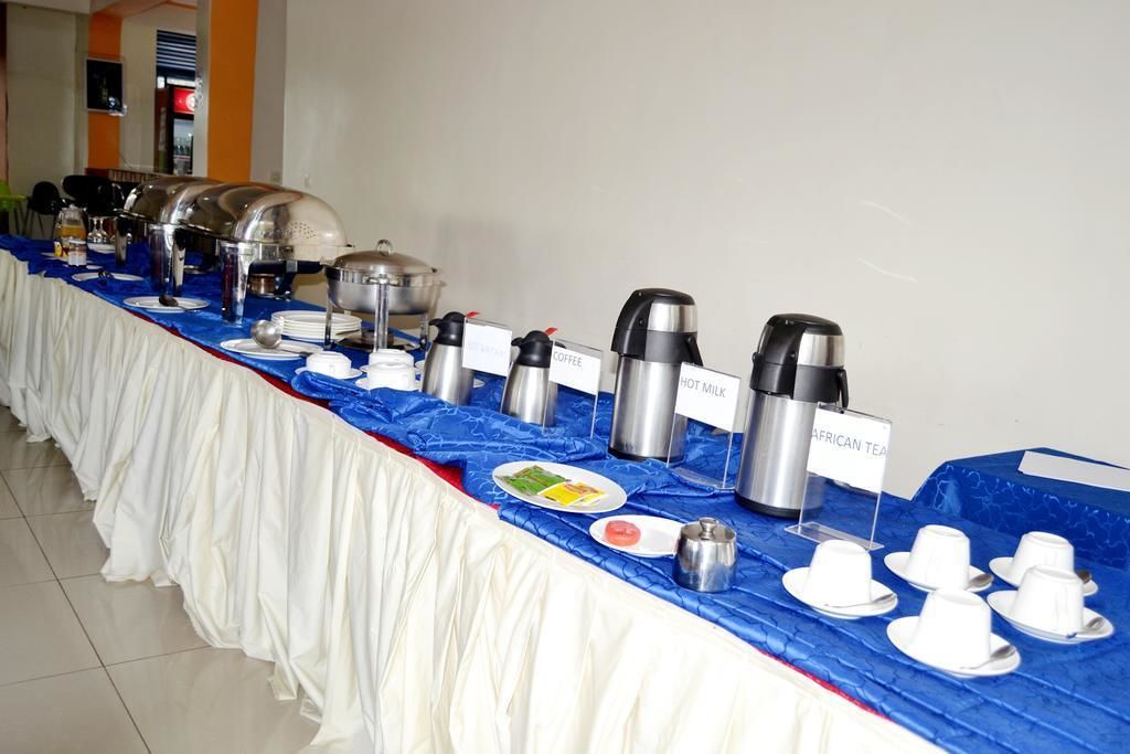 A buffet table with labeled coffee, hot milk, and African tea dispensers, plates, and cups.