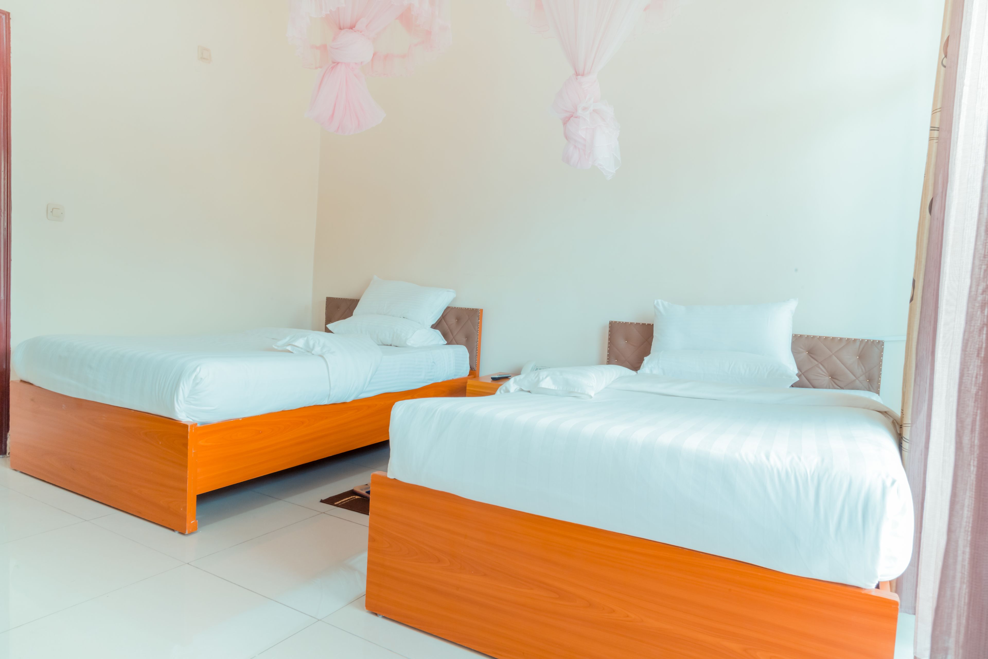 Two single beds with wooden frames and white bedding in a room with white walls and a tiled floor.