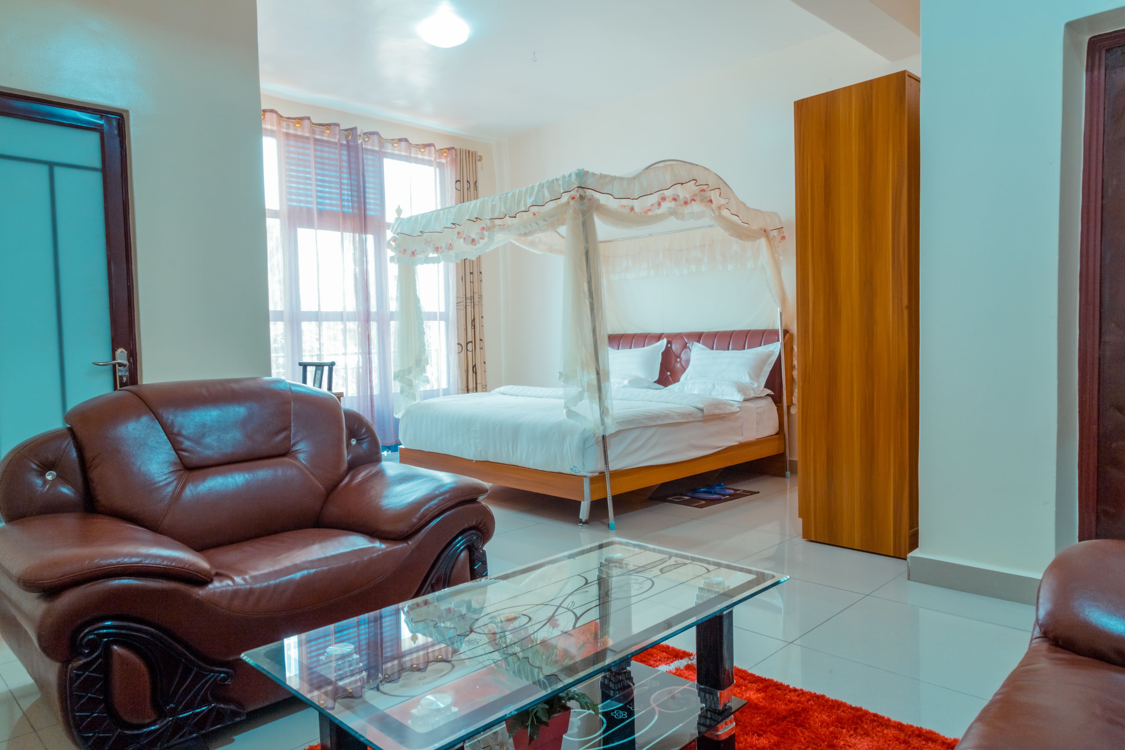 A bedroom with a four-poster bed, a leather armchair, and a glass coffee table.