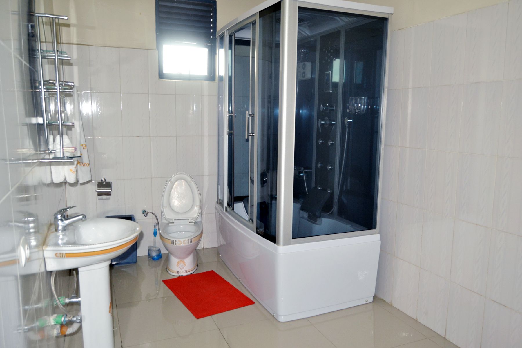 Un baño moderno con ducha de vidrio, inodoro, lavamanos y una alfombra de baño roja.