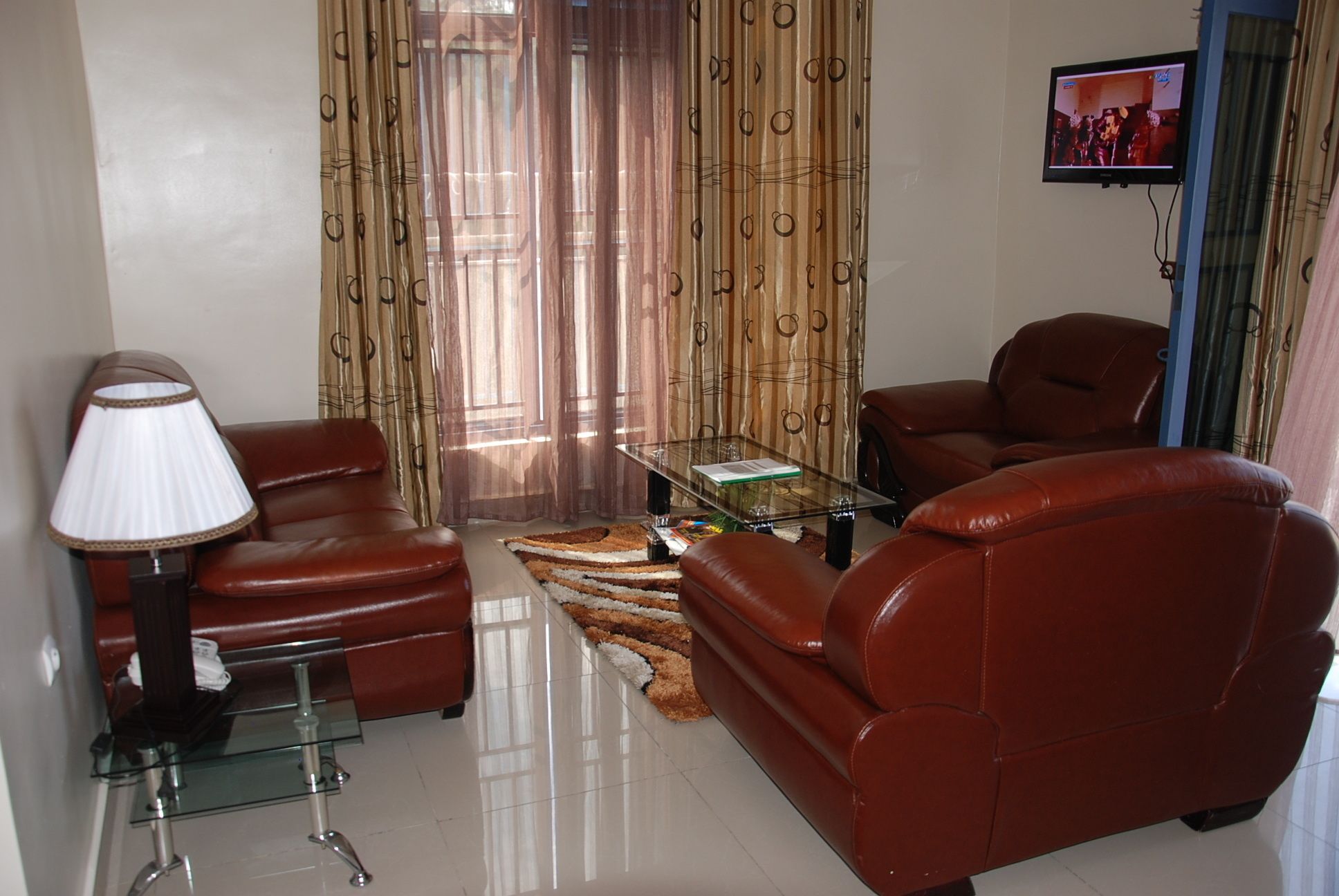 A living room with leather sofas, a glass coffee table, a lamp, and a TV on the wall.