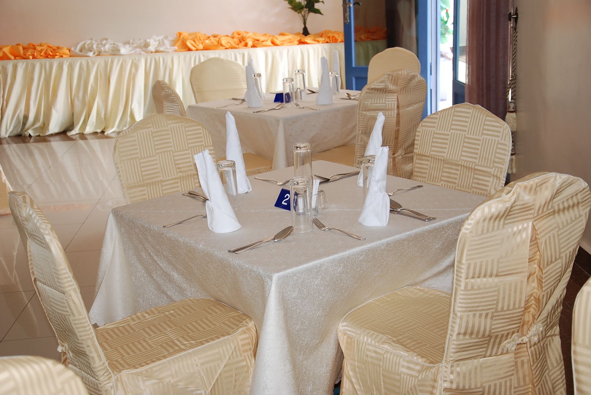 A dining area with round tables, white tablecloths, and wicker chairs.
