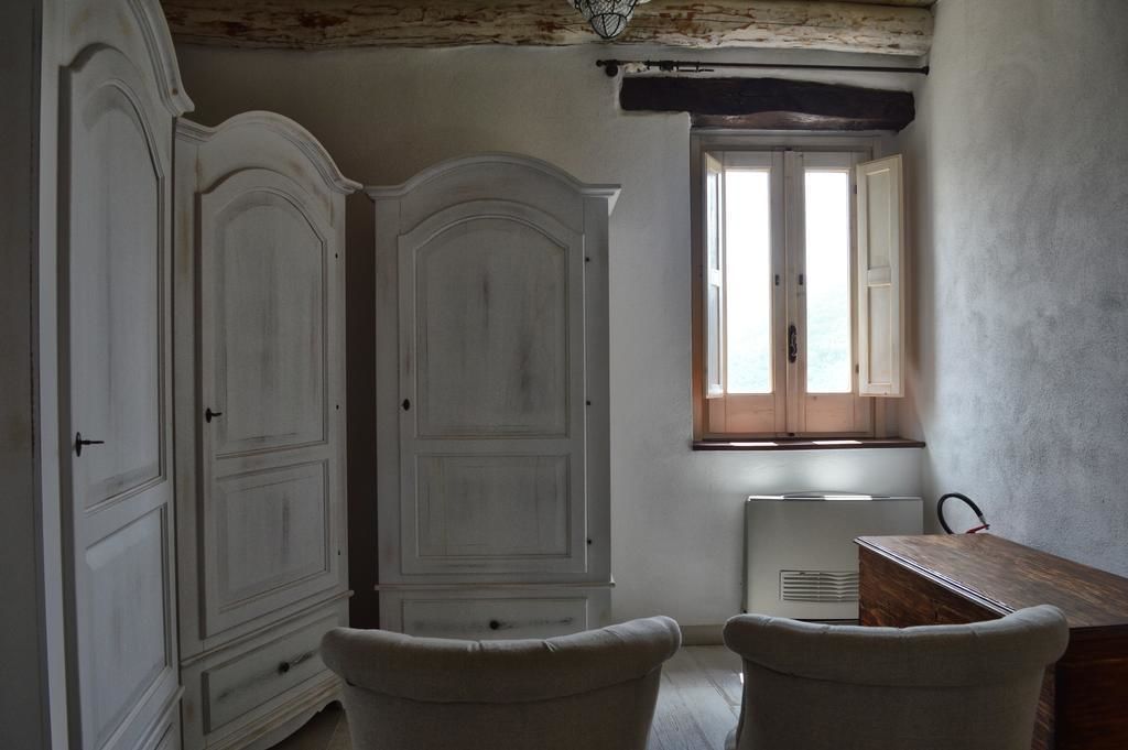 A room with a large white wardrobe, a small table, and a window with wooden shutters.