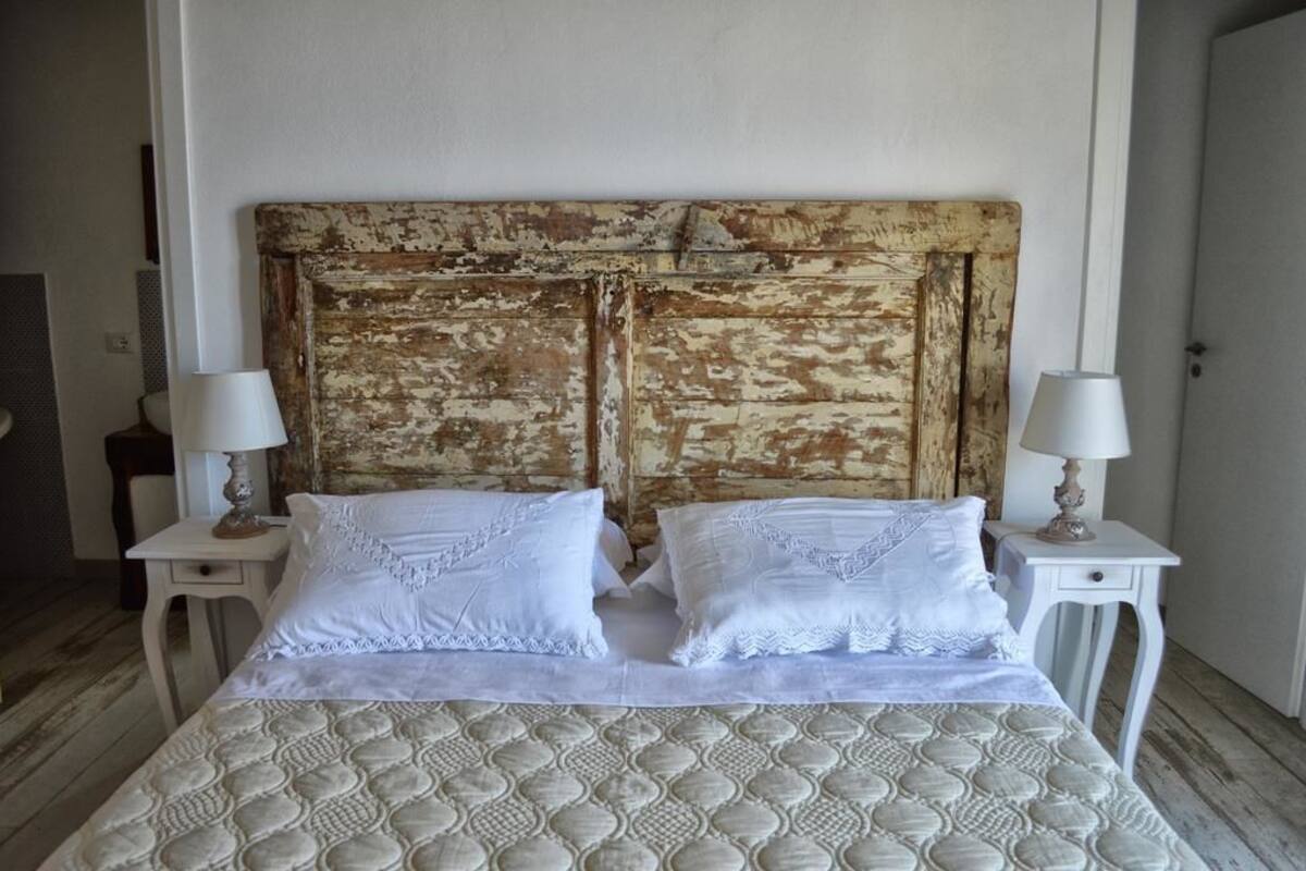 A bed with a textured white bedspread, two matching pillows, and a rustic wooden headboard. There are two bedside tables with lamps.