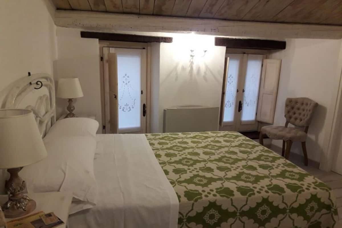 A bedroom with a bed, a chair, a nightstand, and a lamp.