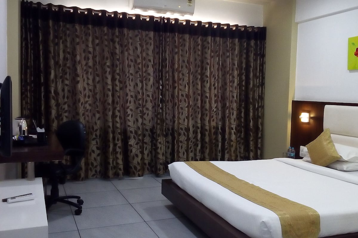 Ein Hotelzimmer mit einem Bett, einem Schreibtisch mit Stuhl, einem Vorhang und einer Wandleuchte.