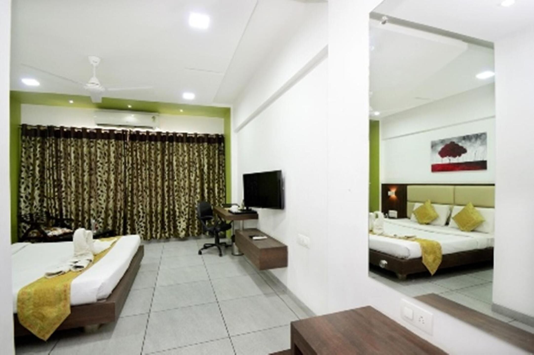A hotel room with two beds, a desk, a chair, a TV, and a ceiling fan.