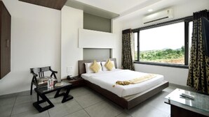 Quarto de hotel moderno com uma cama grande, uma escrivaninha e uma janela com cortinas.