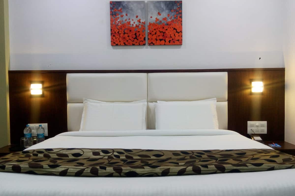 Ein Hotelzimmer mit einem großen Bett, zwei Wandleuchten, einem Nachttisch mit Telefon und einer Wasserflasche.
