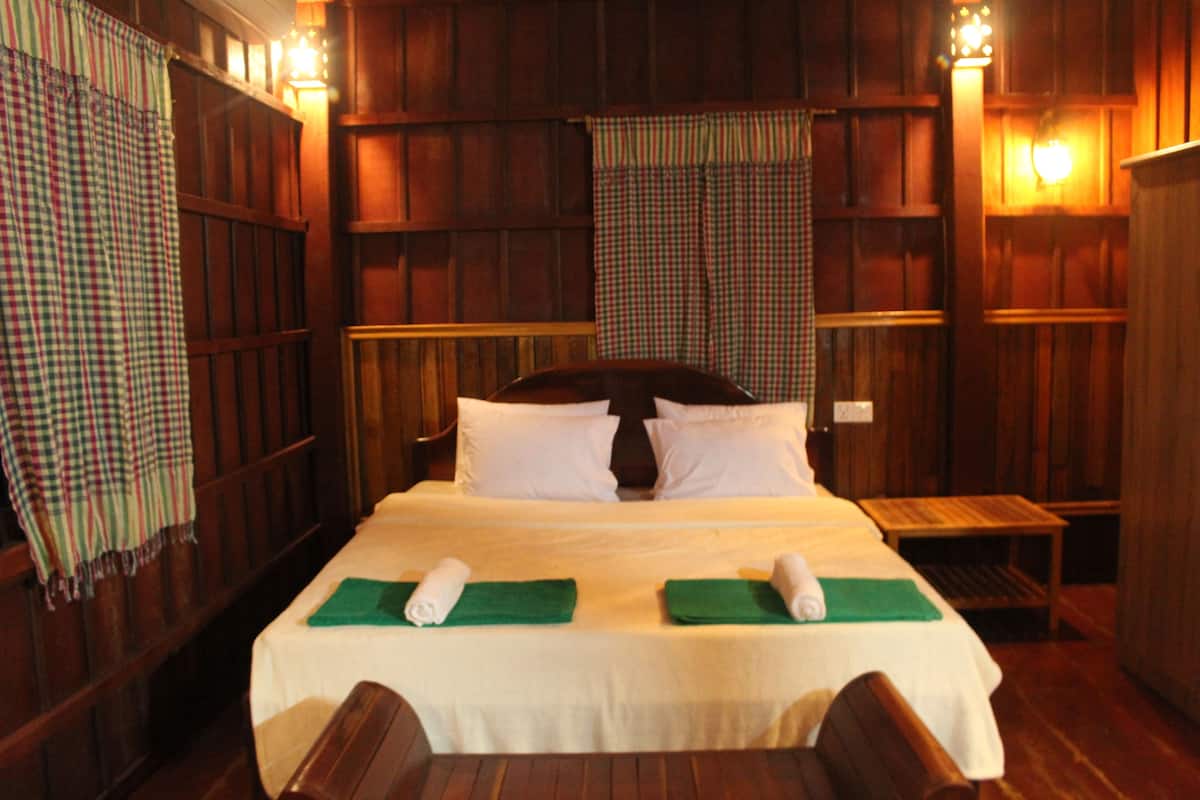 A room with a large bed, wooden paneling, and a checkered curtain.