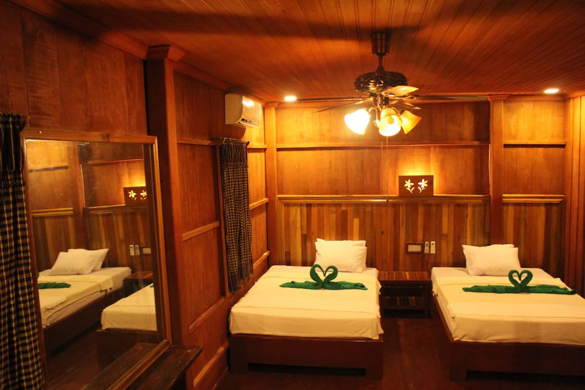 A room with two beds, wooden walls, a ceiling fan, and a mirror.