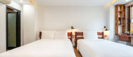 Une chambre d’hôtel avec deux lits simples, des têtes de lit en bois, un petit bureau avec une lampe, un miroir et une étagère en bois ornée d’objets décoratifs.