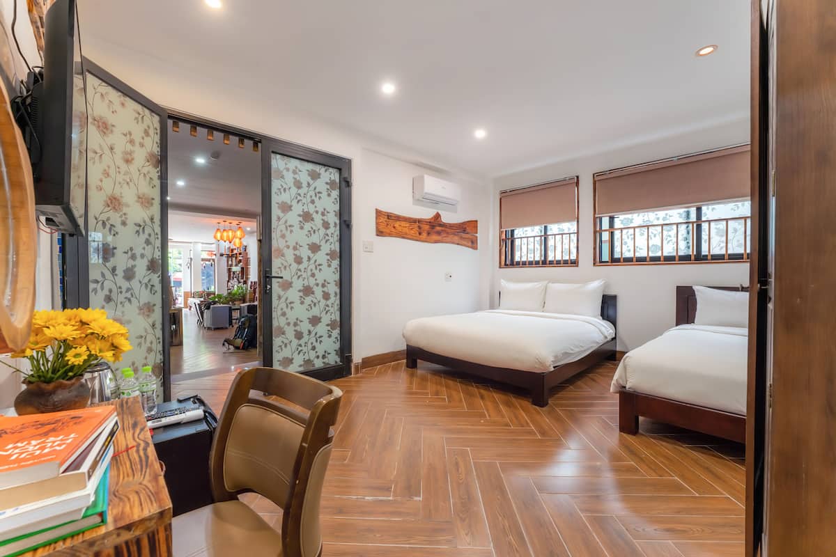 Une chambre d’hôtel avec deux lits, un bureau avec une chaise, un plancher en bois et une vue sur l’extérieur grâce à de grandes fenêtres.