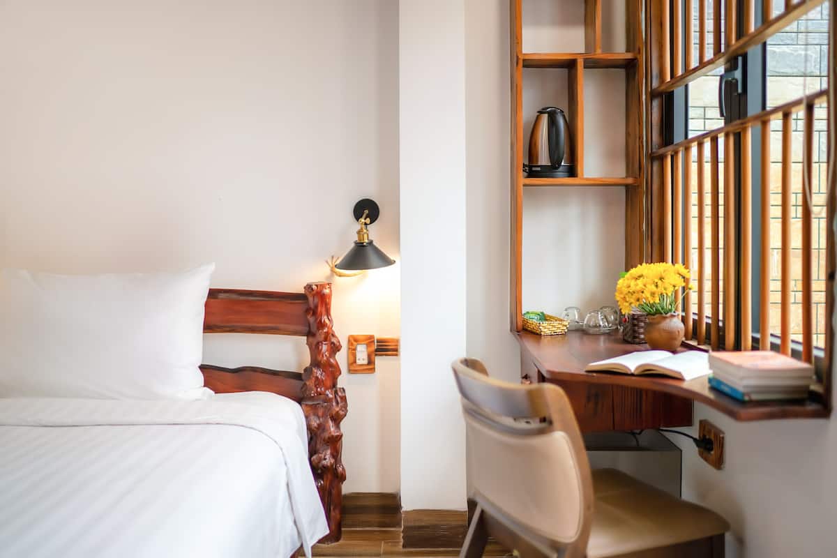 Une chambre d’hôtel avec un lit, un bureau et une chaise, une lampe et une fenêtre donnant sur un paysage agréable.