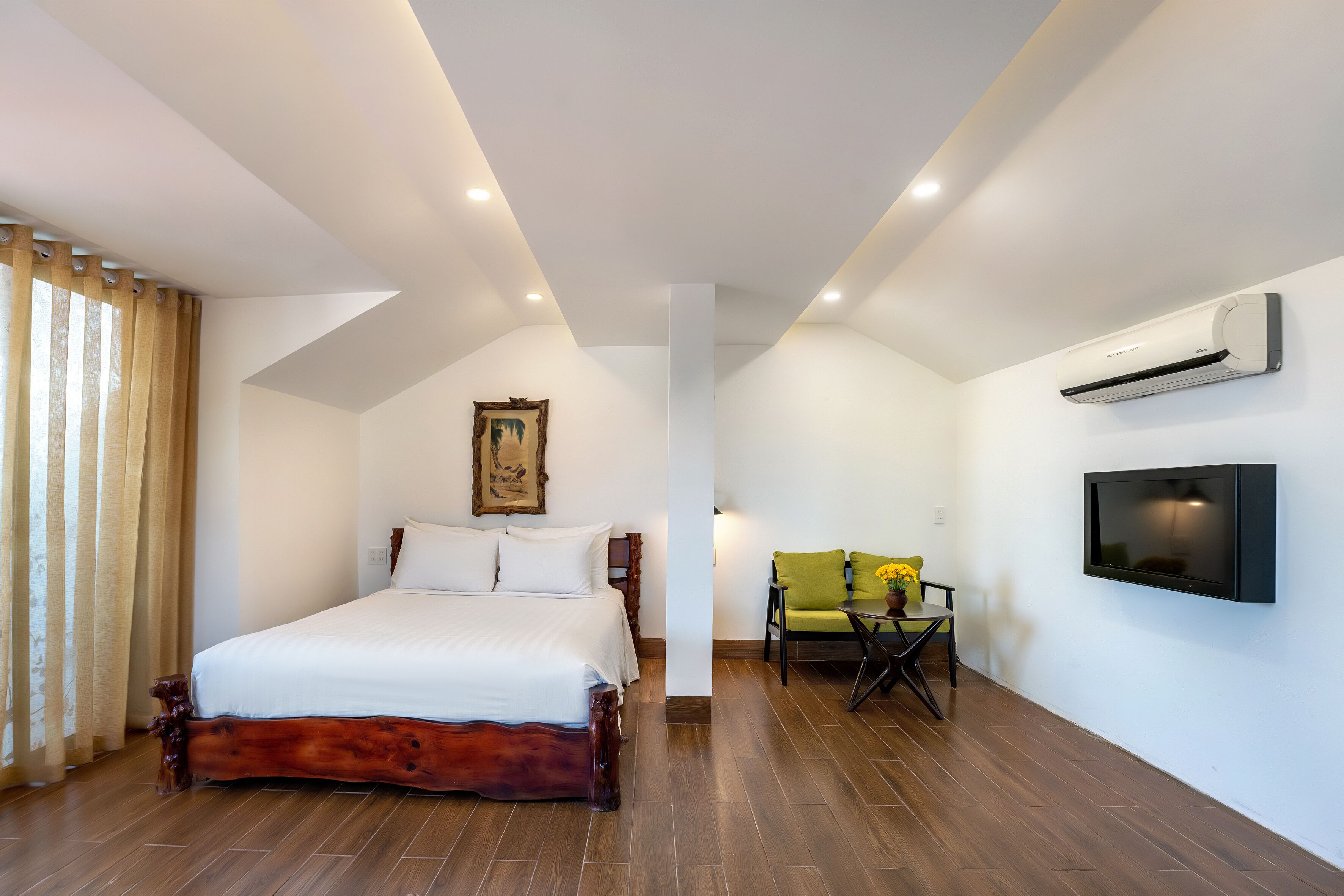 Quarto com cama de madeira, televisão fixada na parede e uma cadeira com almofada.
