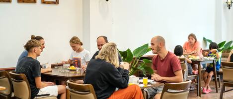Eine Gruppe von Menschen speist in einem Restaurant mit Holztischen und -stühlen, Bilderrahmen an der Wand und einem Blumentopf.