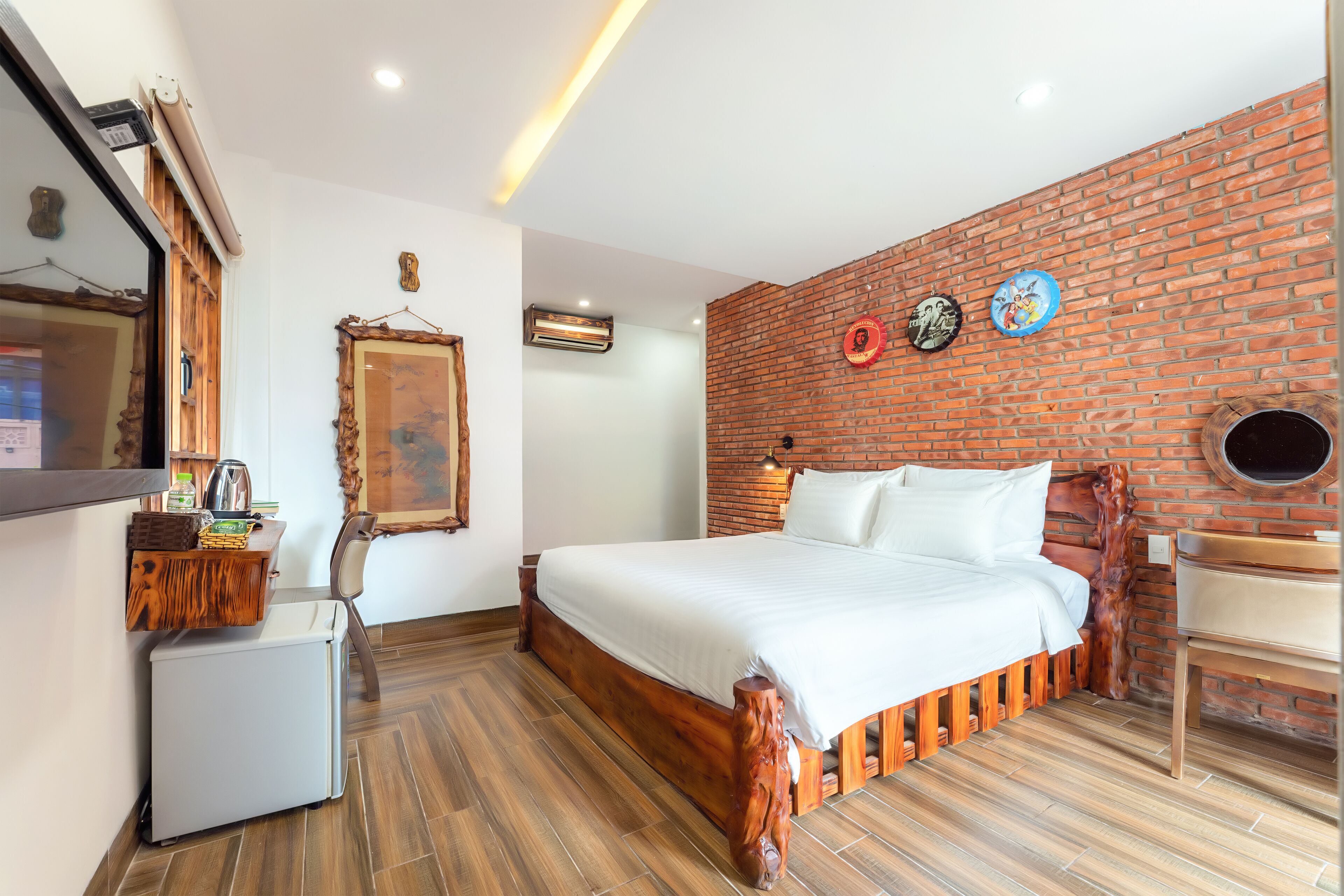 A bedroom with a brick wall, a bed, a small refrigerator, and a wooden chair.