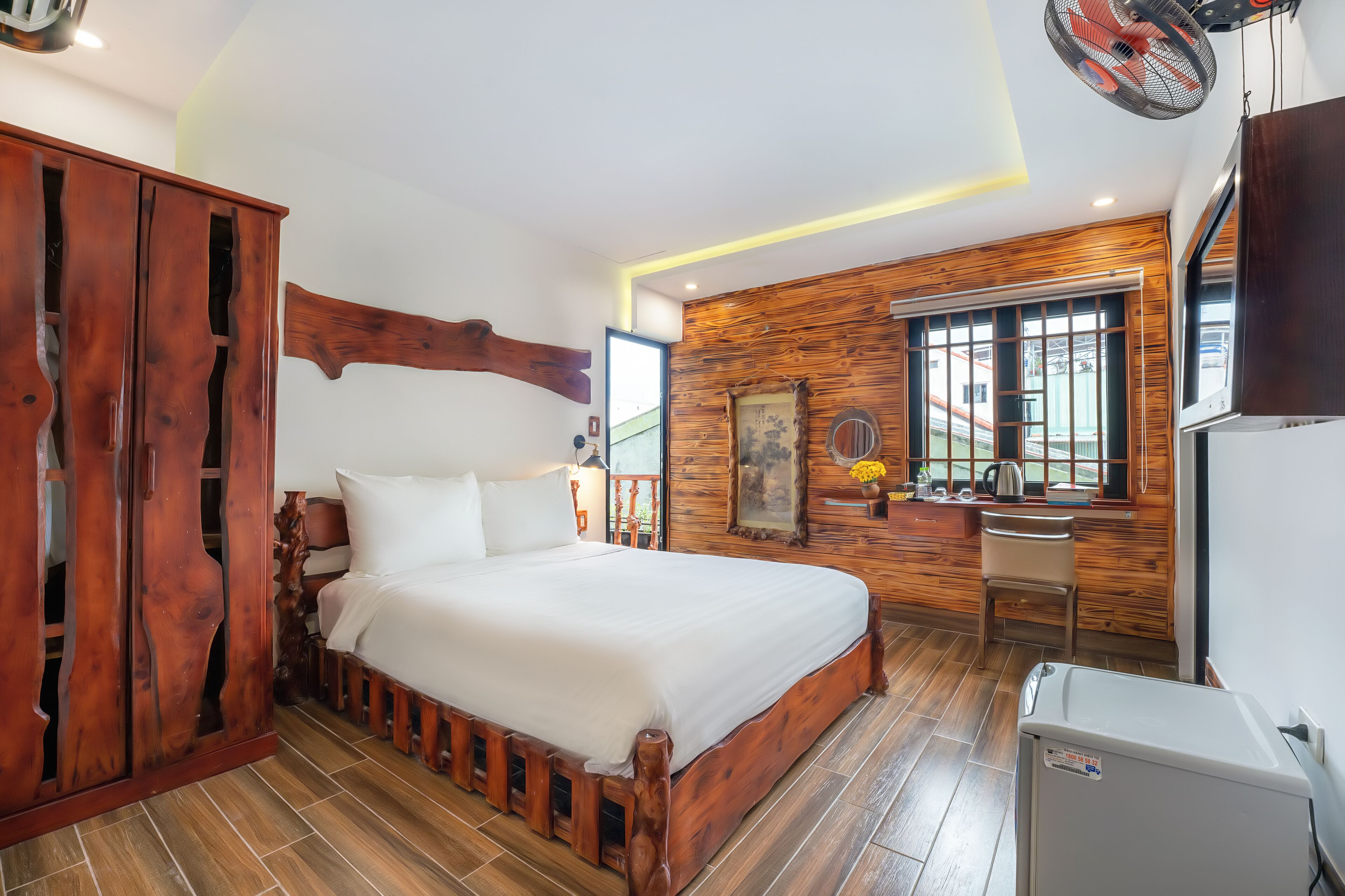Een slaapkamer met een houten bedframe, een bureau en een koelkast.