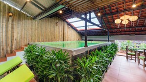 Un espacio interior moderno con pared de bambú, asientos verdes y zona de piscina.