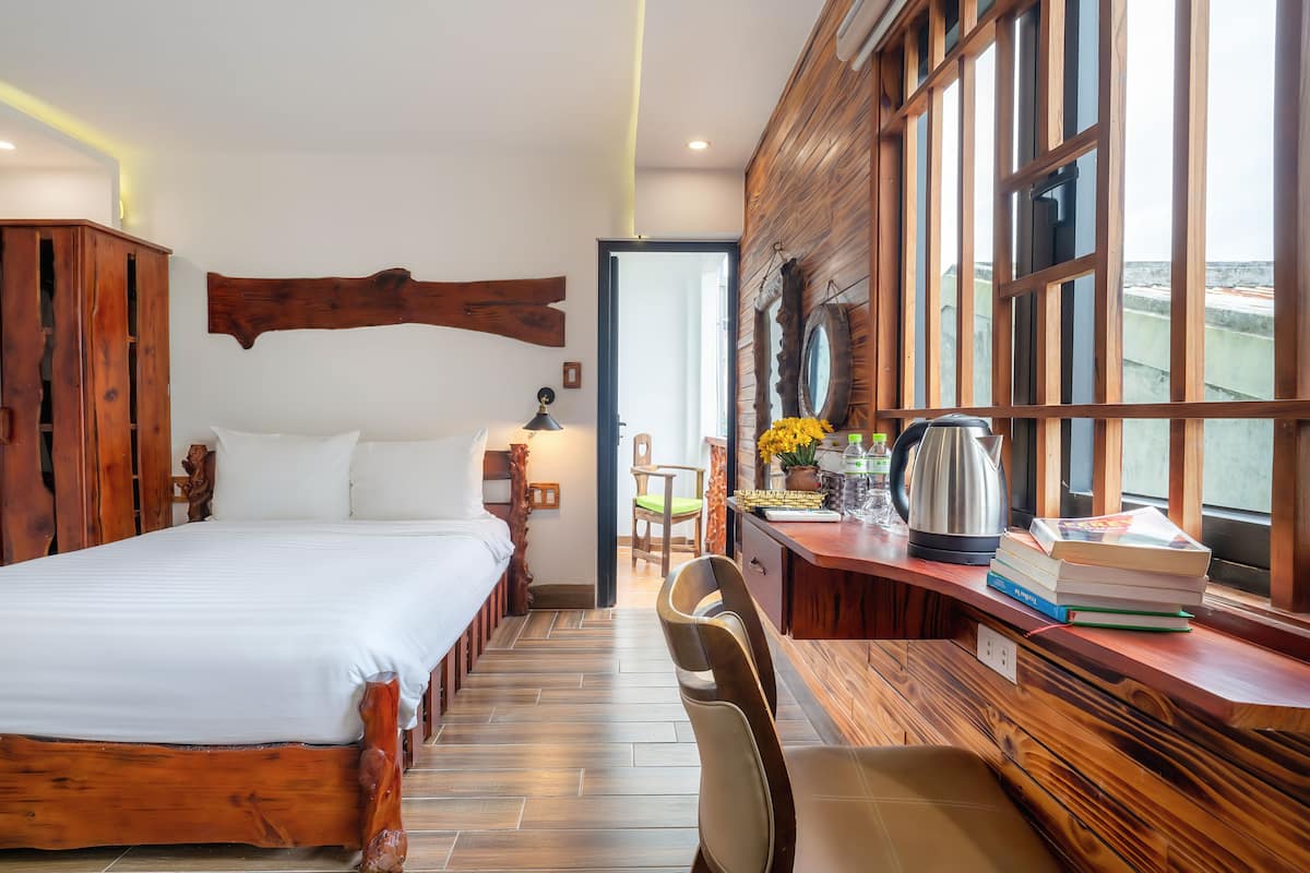 Une chambre avec un lit en bois, un bureau avec des livres et une bouilloire, et une vue dégagée grâce à de grandes fenêtres.