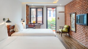 Habitación de hotel con una cama grande, un escritorio con una silla, un televisor montado en una pared de ladrillo y un balcón con vistas.