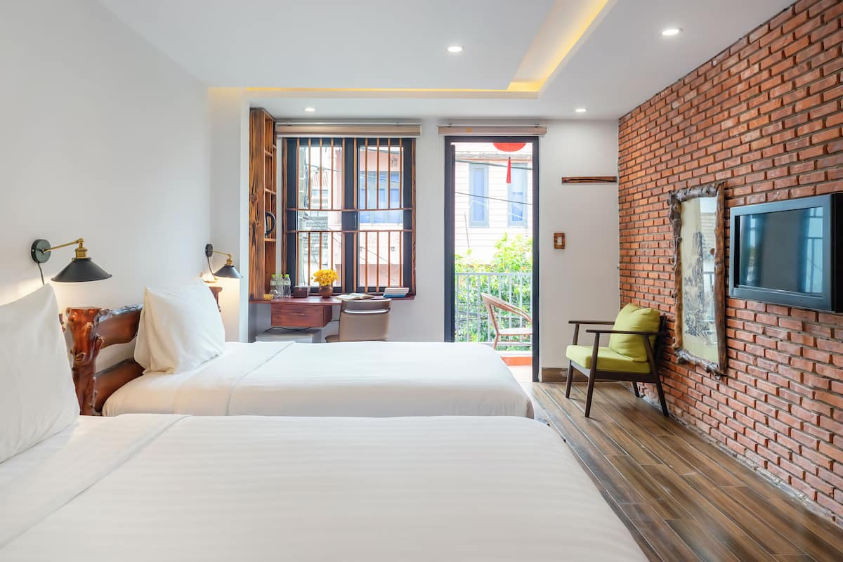 Une chambre d’hôtel avec un grand lit, un bureau avec une chaise, un téléviseur fixé au mur en briques et un balcon avec vue.