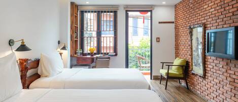 A hotel room with a large bed, a desk with a chair, a TV mounted on a brick wall, and a balcony with a view.