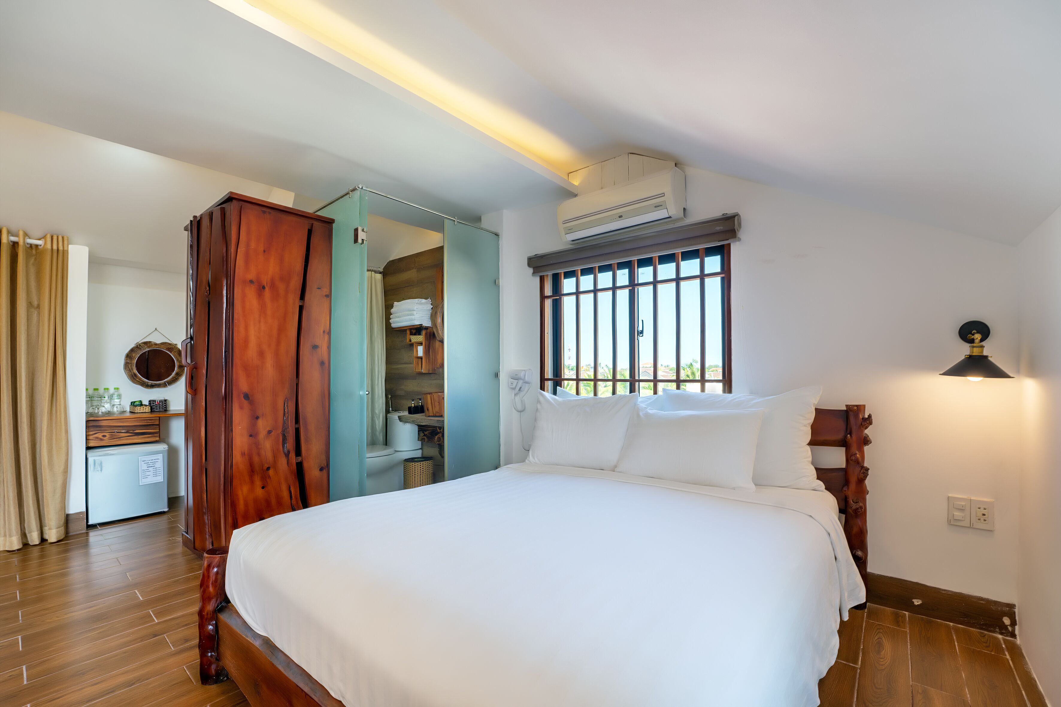 A neatly arranged bedroom with a large bed, a wardrobe, a desk with a mirror, and a window with bars.