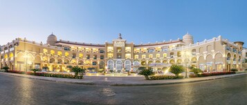 Un hotel amplio y bien iluminado con múltiples balcones y ventanas de arco, que cuenta con una fuente central y jardines ajardinados.