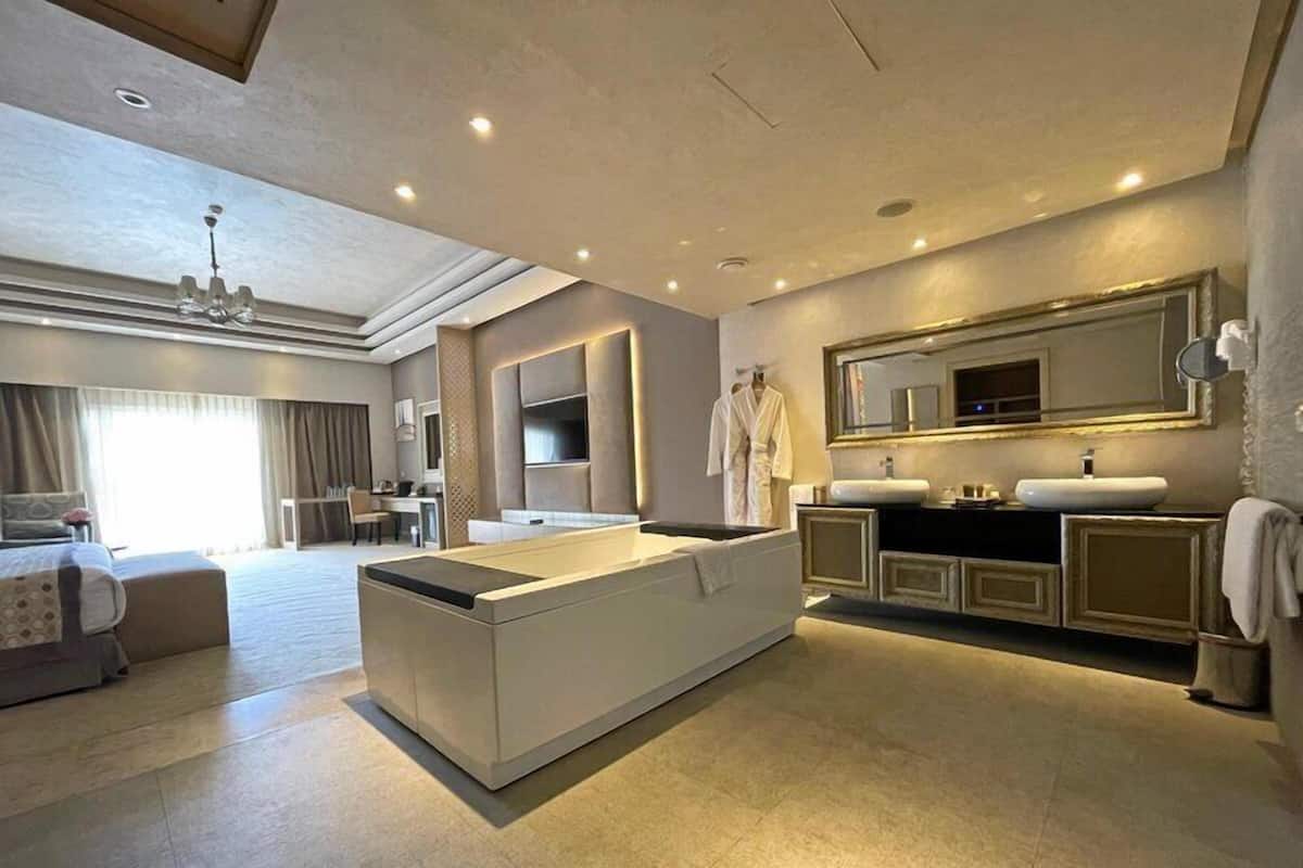 Une chambre d’hôtel moderne dotée d’un grand îlot central, d’un coin salon séparé, d’une table à manger et d’une salle de bain bien équipée.