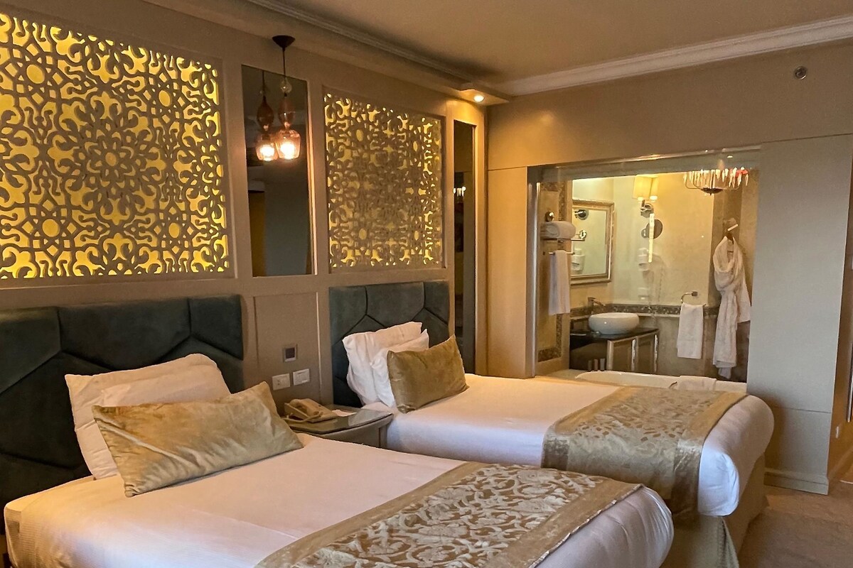 A hotel room with two beds, a large mirror, and a bathroom visible through an open door.