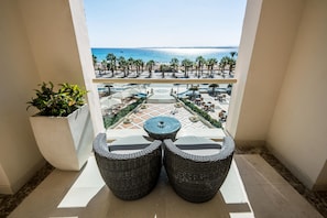 Un balcon agrémenté de meubles en osier, d’une plante en pot et offrant une vue sur la plage et l’espace piscine.