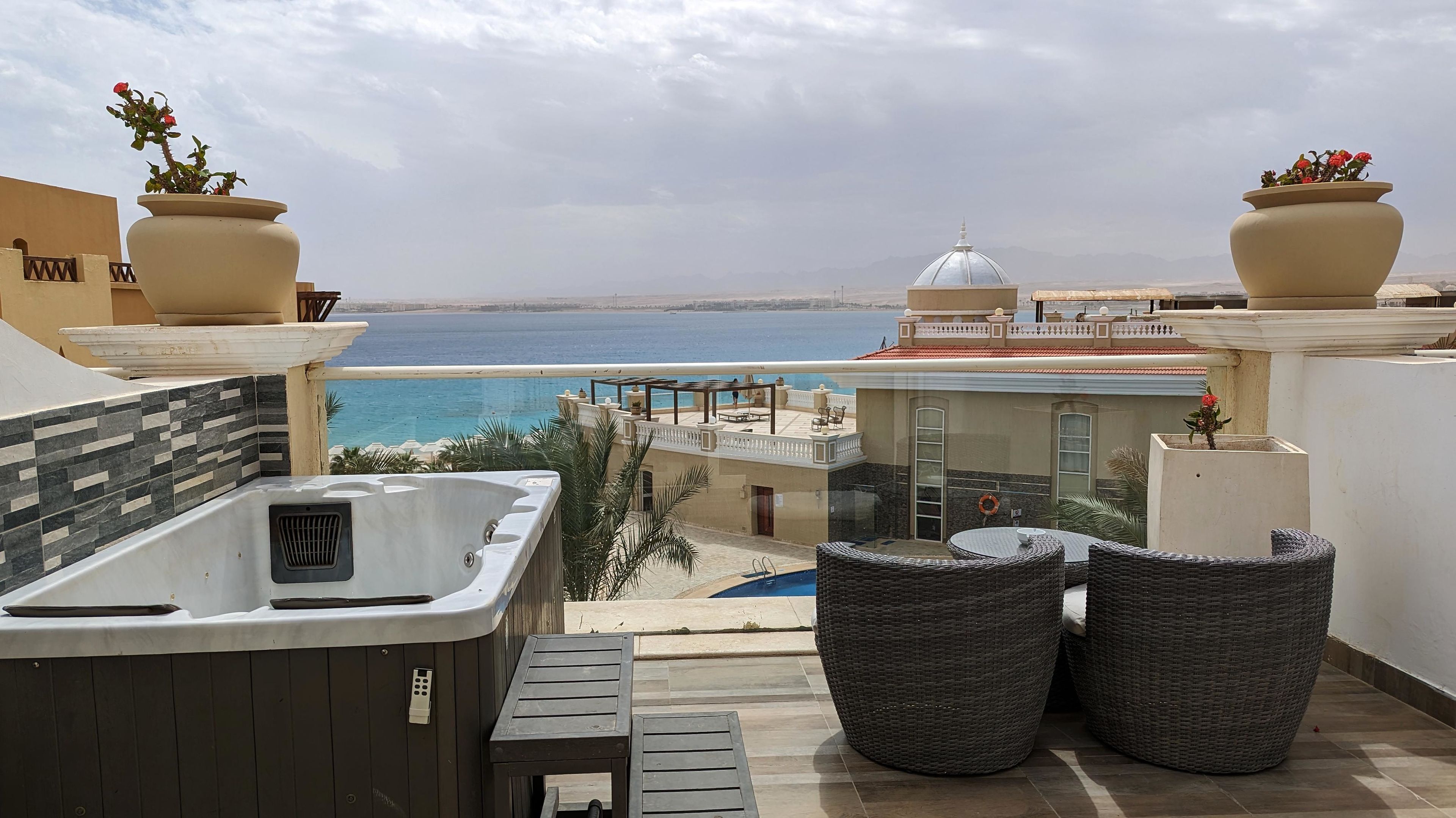 A balcony with a hot tub, wicker chairs, and a view of the sea.