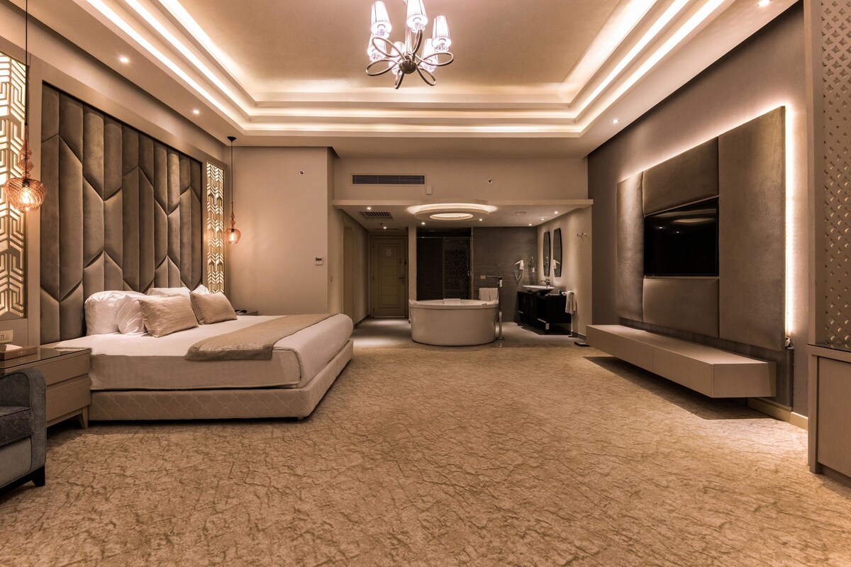 A modern bedroom with a large bed, a vanity, and a television.