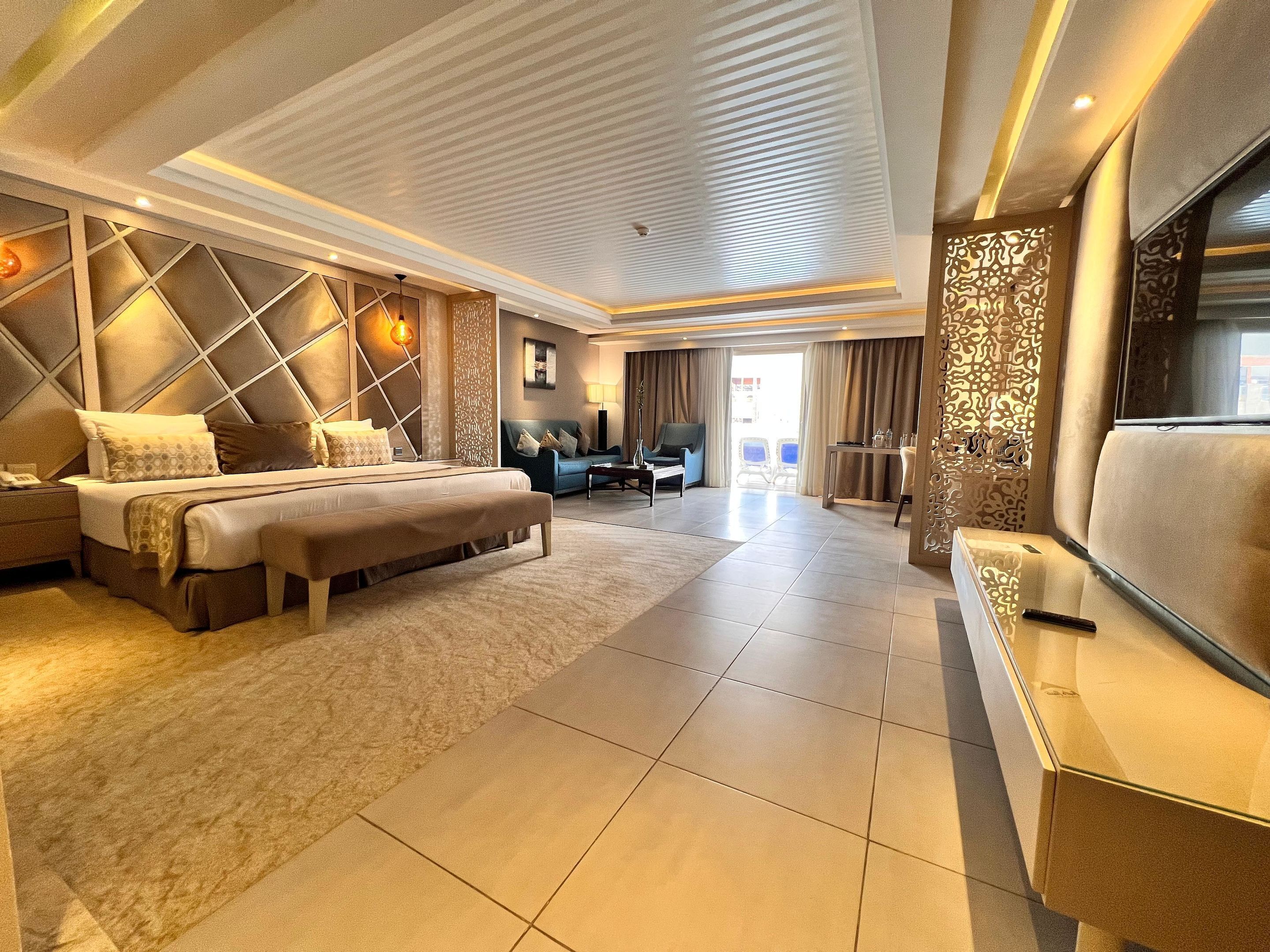 A modern hotel room with a large bed, a seating area, and a TV.