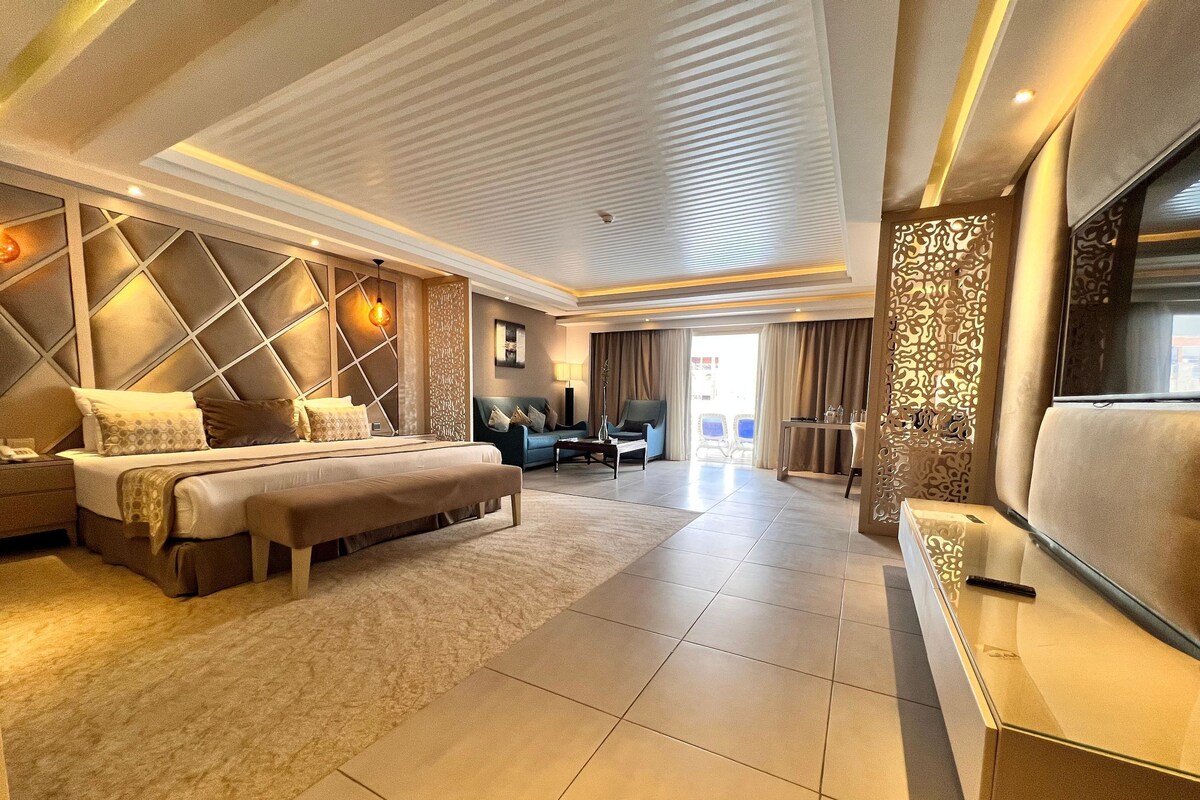 A modern hotel room with a large bed, a seating area, and a TV.