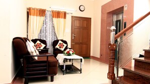 A living room with a sofa, a small table with a flower, and a staircase. - Ayur Bethaniya Ayurveda Hospital (Talappilly)