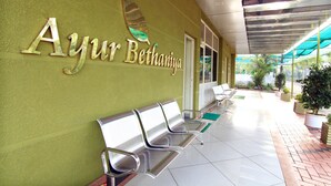 A reception area with a green wall, a sign reading "Ayur Bethaniya," and three metal benches. - Ayur Bethaniya Ayurveda Hospital (Talappilly)