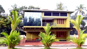 A two-story building with a balcony, surrounded by palm trees and greenery. - Ayur Bethaniya Ayurveda Hospital (Talappilly)