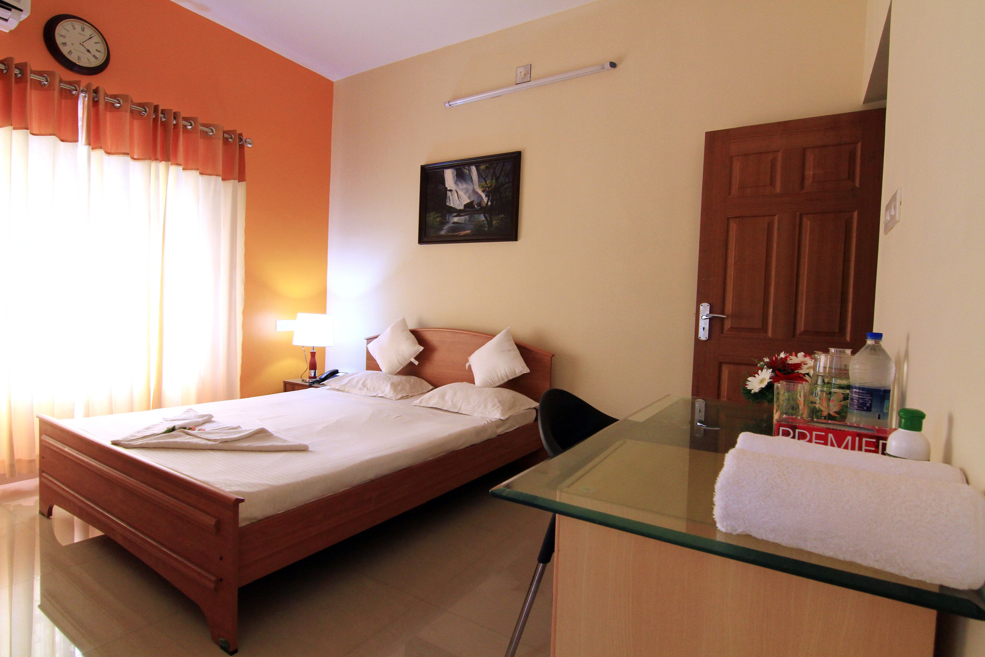 A hotel room with a bed, a desk, a chair, a lamp, a painting on the wall, and a door.