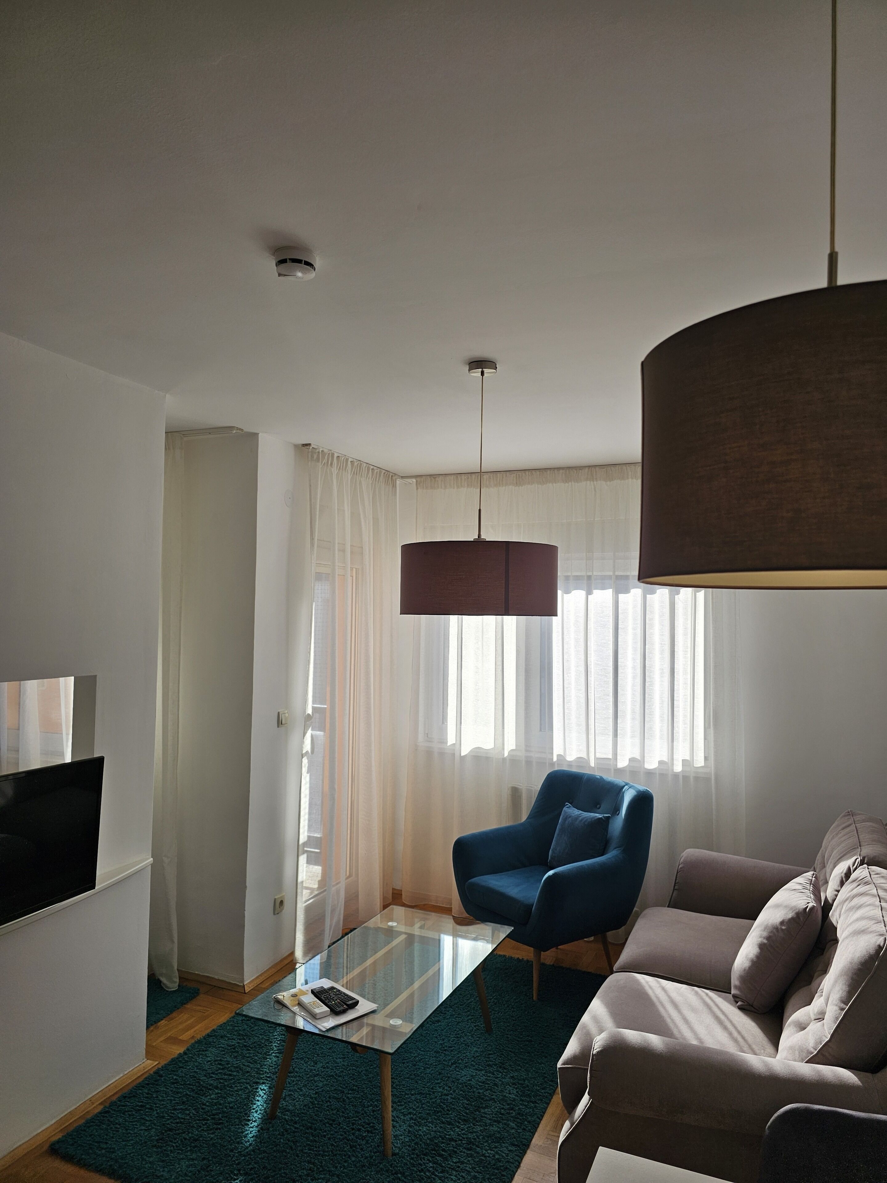 A modern living room with a glass coffee table, a blue armchair, a brown sofa, and a large pendant light.