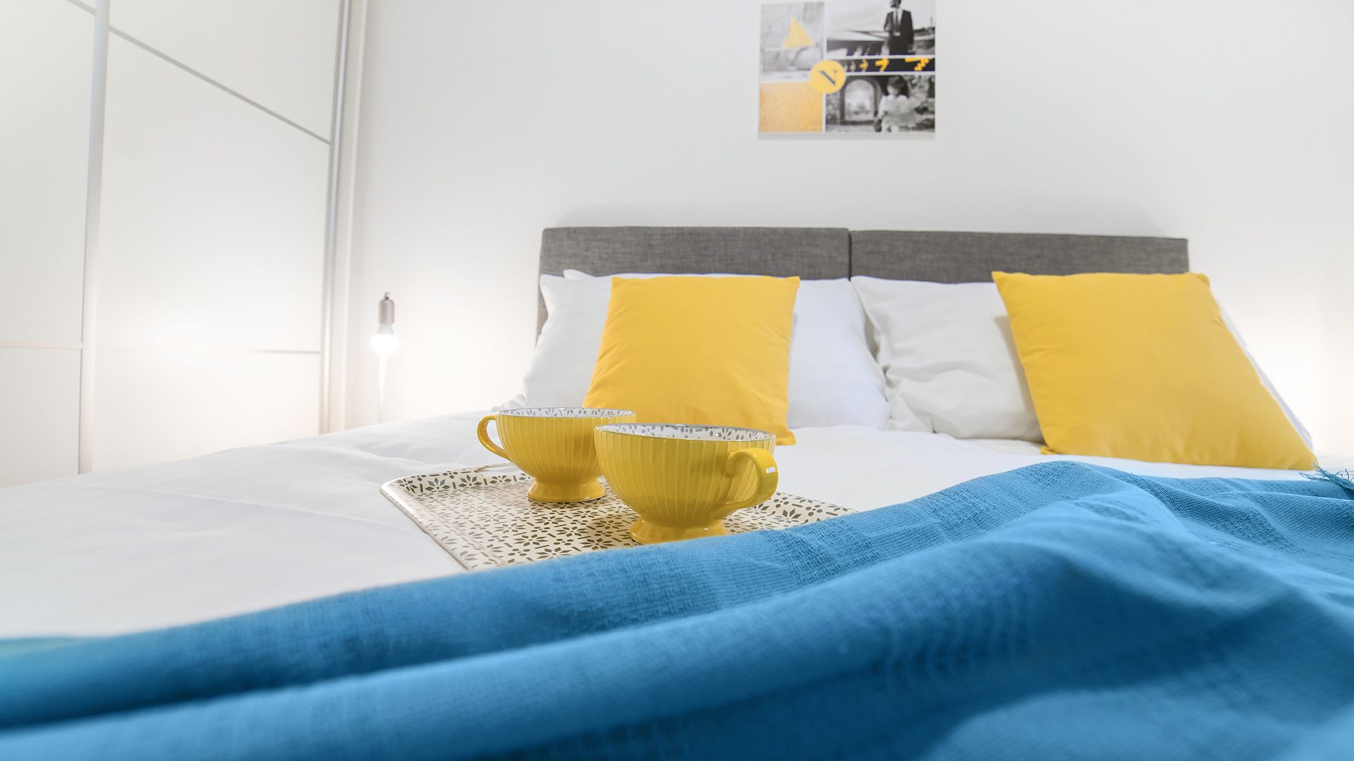 A neatly made bed with a white and gray headboard, two yellow pillows, and a blue blanket.
