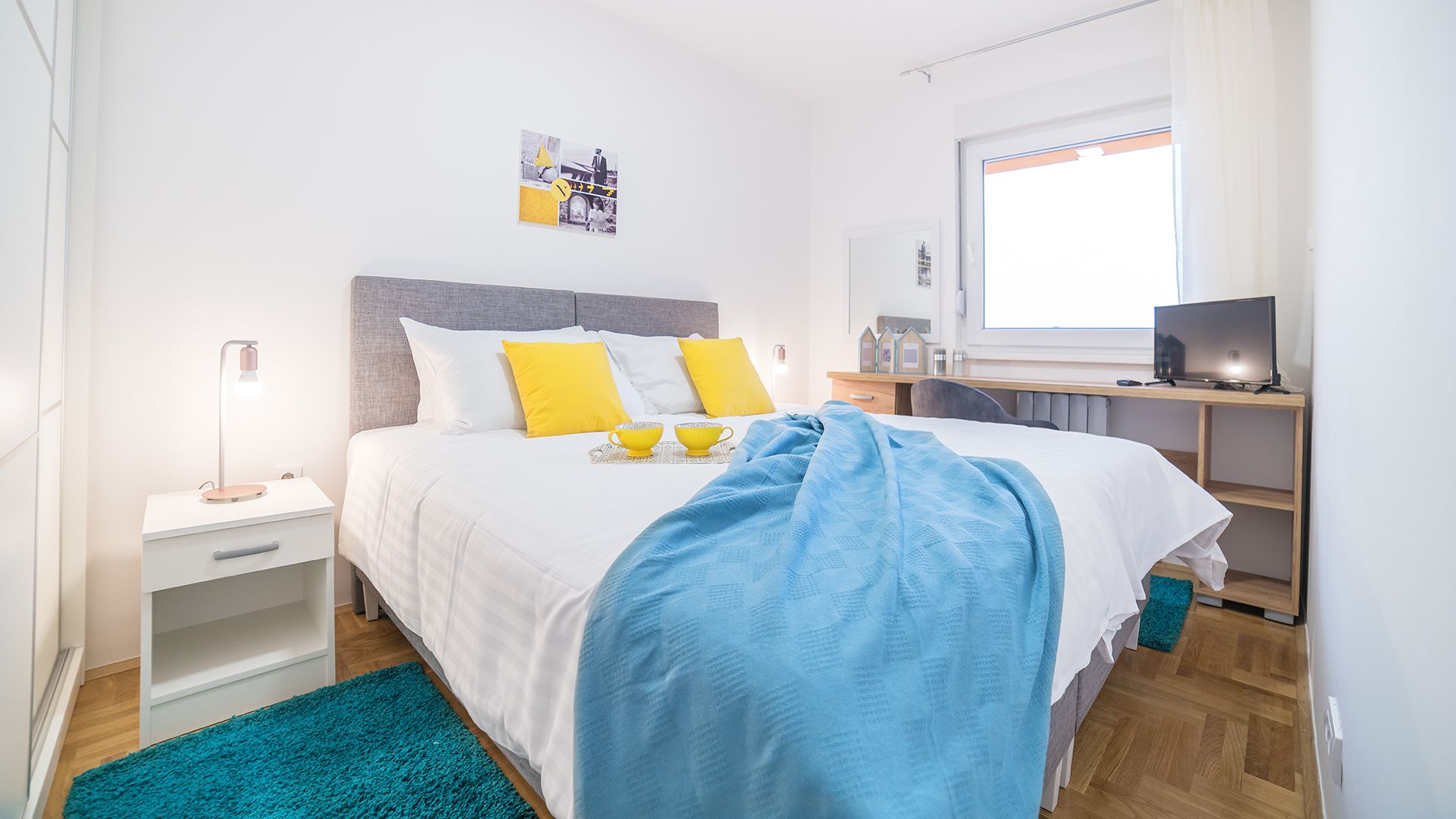 A bedroom with a bed, bedside table, lamp, and a desk with a computer.