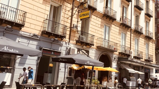 Une rue avec des terrasses et un immeuble doté de balcons et d’enseignes.