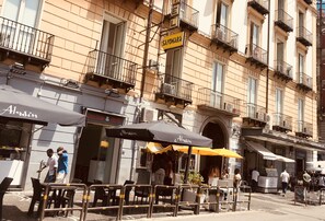 Una calle con mesas al aire libre y un edificio con balcones y señalización.